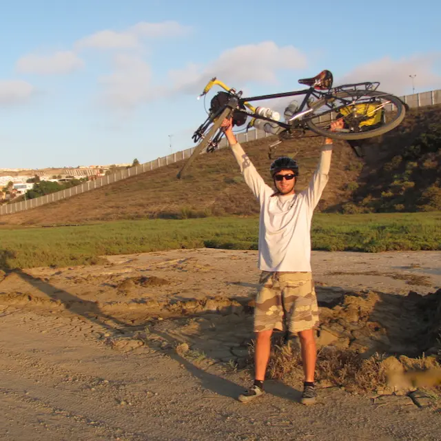 nikolas osvalds holding his bike above his head at the mexican border