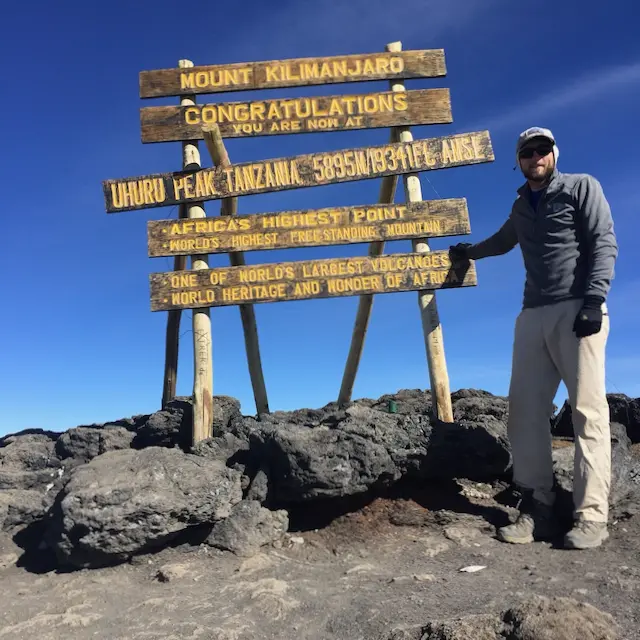 nikolas osvalds posing at the summit sign of mount kilimanjaro